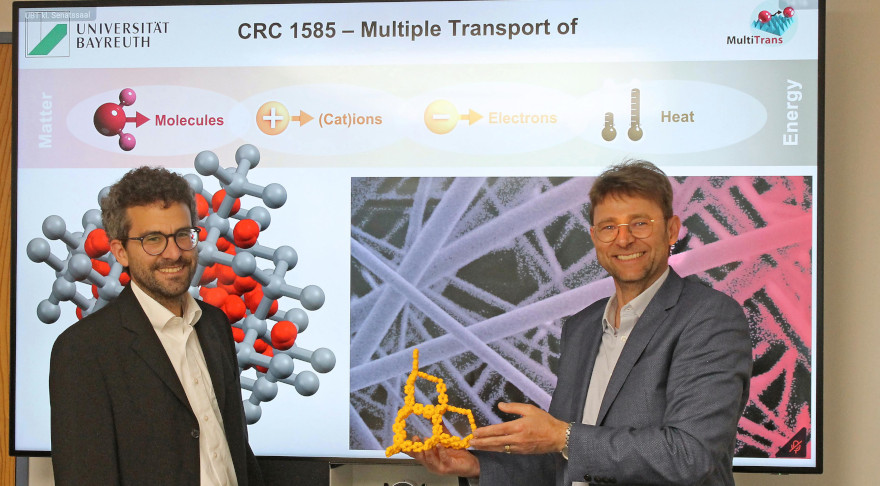 Prof. Dr. Jürgen Senker (re.) und Prof. Dr. Markus Retsch (li) von der Universität Bayreuth mit einem 3D-gedruckten Modell der Porosität von kovalent-organischen Netzwerken (in der Mitte, gelb) (© UBT / Chr. Wißler)