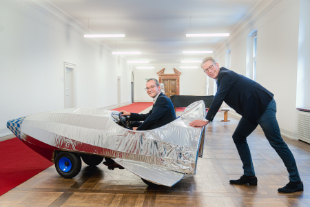 Wissenschaftsminister Markus Blume (r.) mit Prof. Dr.-Ing. Bastian J. M. Etzold in einer Seifenkiste, die als Requisit in einem Videoclip zur Hightech Agenda Bayern verwendet wurde (© Axel König/StMWK)