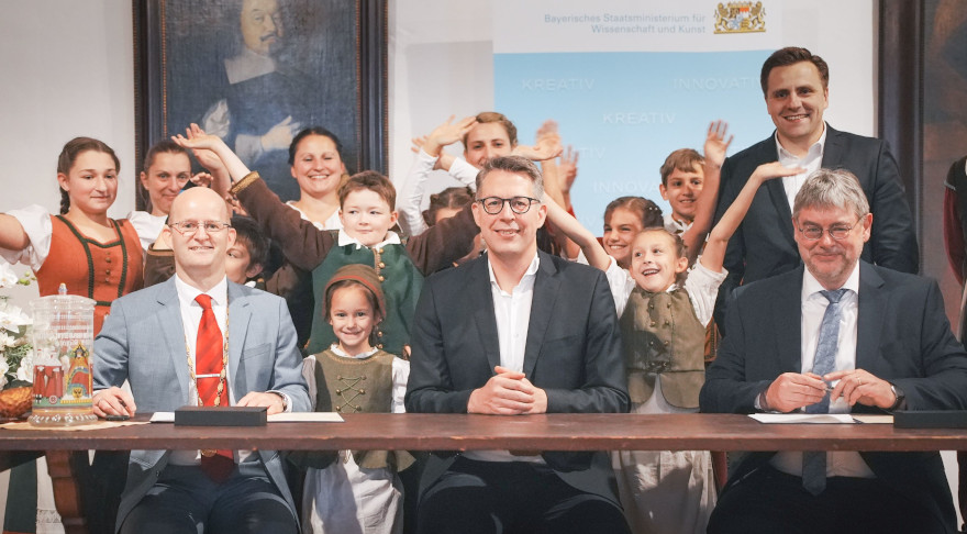 Kunstminister Blume (Mi.) mit Rothenburgs Oberbürgermeister Dr. Markus Naser (l.) und dem stellv. Direktor des Hauses der Bayerischen Geschichte Dr. Peter Wolf (r.) bei der Vertragsunterzeichnung. Im Hintergrund: Mitwirkende des Festspiels „Der Meistertrunk“ e.V. und MdL Andreas Schalk (© Axel König/StMWK)