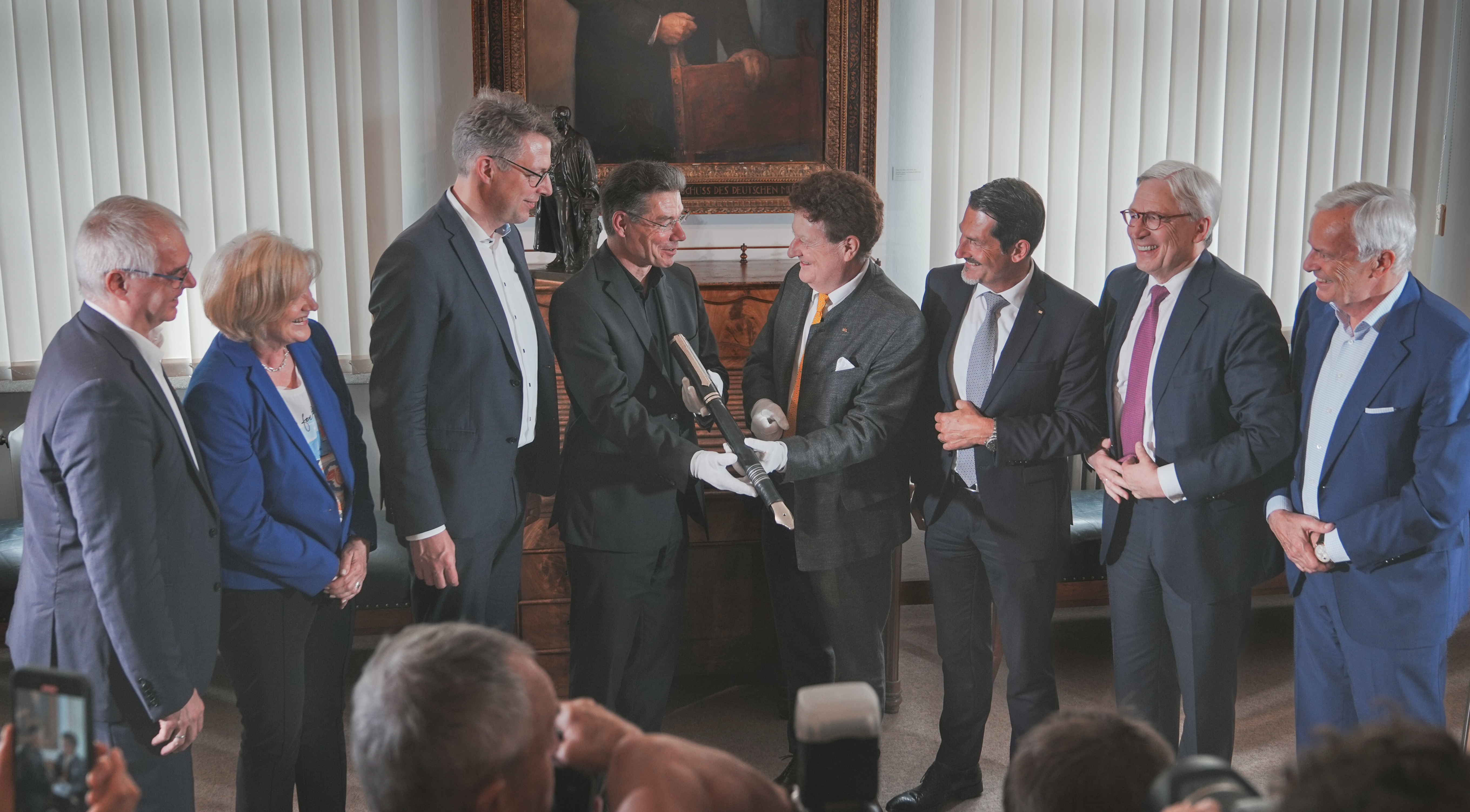 Im Beisein von Bayerns Wissenschaftsminister Markus Blume (3. v. l.) und TUM-Präsident Thomas F. Hofmann (3. v. r.) übergibt Wolfgang M. Heckl (4. v. r.) den Staffelstab in Form eines überdimensionalen Füllfederhalters aus der Museumssammlung an Michael Decker (4. v. l.), den neuen Generaldirektor des Deutschen Museums. (© Axel König)